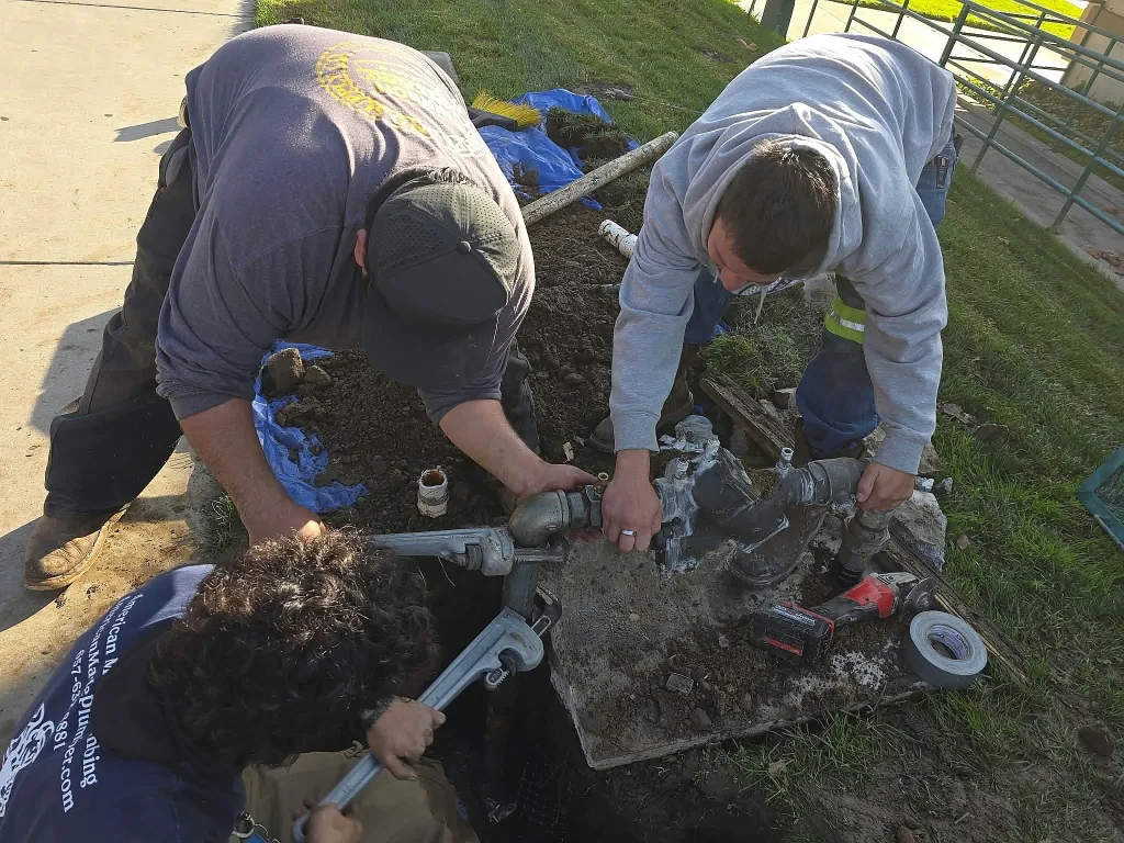 Two technicians fitting a new water valve in an open trench