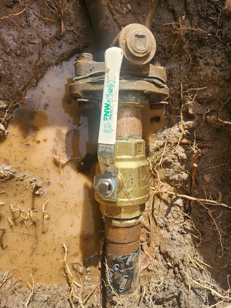 New brass ball valve with a white handle on a water line in an open trench
