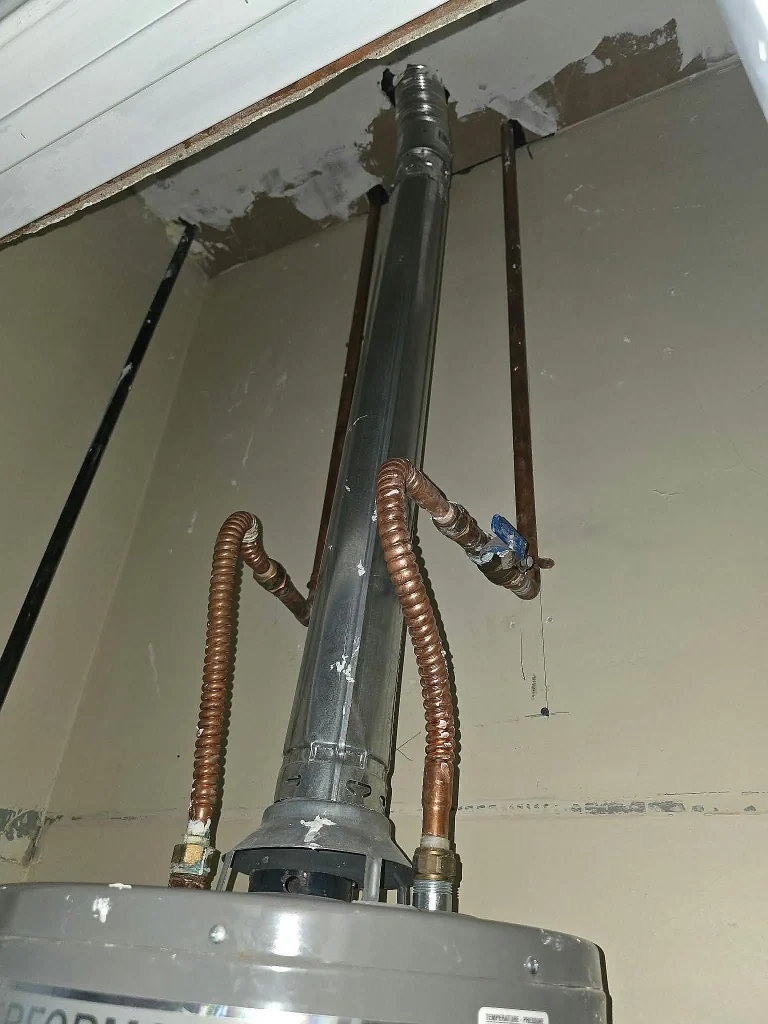 Top of a gas water heater showing its vent pipe and flexible water connections