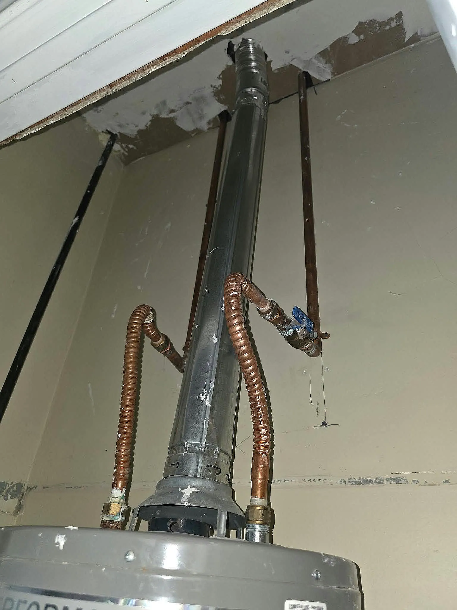 Top of a gas water heater showing its vent pipe and flexible water connections