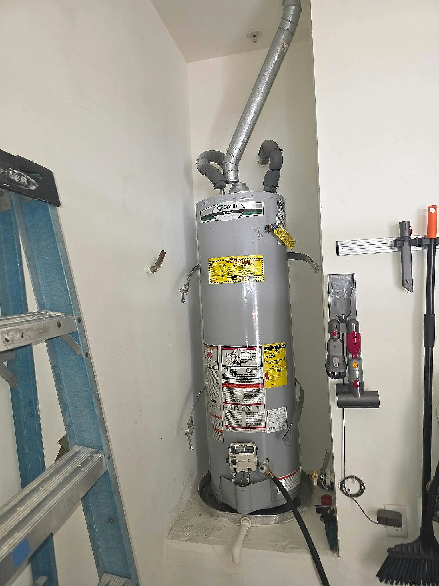 Tank water heater installed in a garage alcove beside a ladder