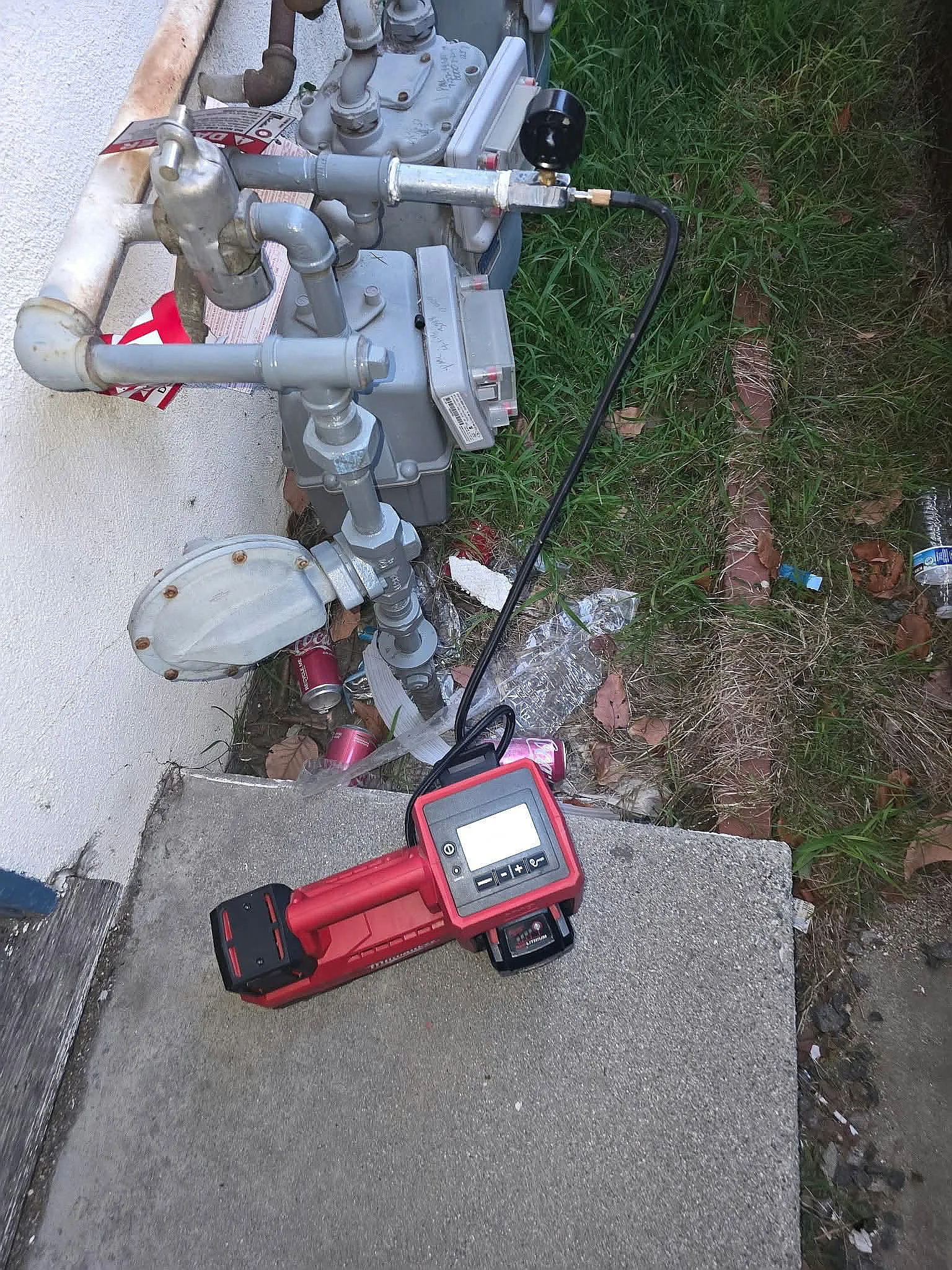 Gas meter piping beside a house with a red gas leak detector on the ground